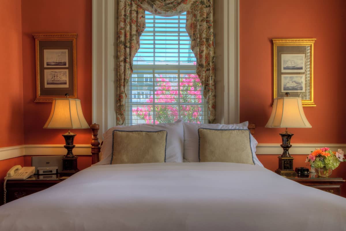 A hotel room with a large bed, two bedside lamps, a telephone, and a window with floral curtains.