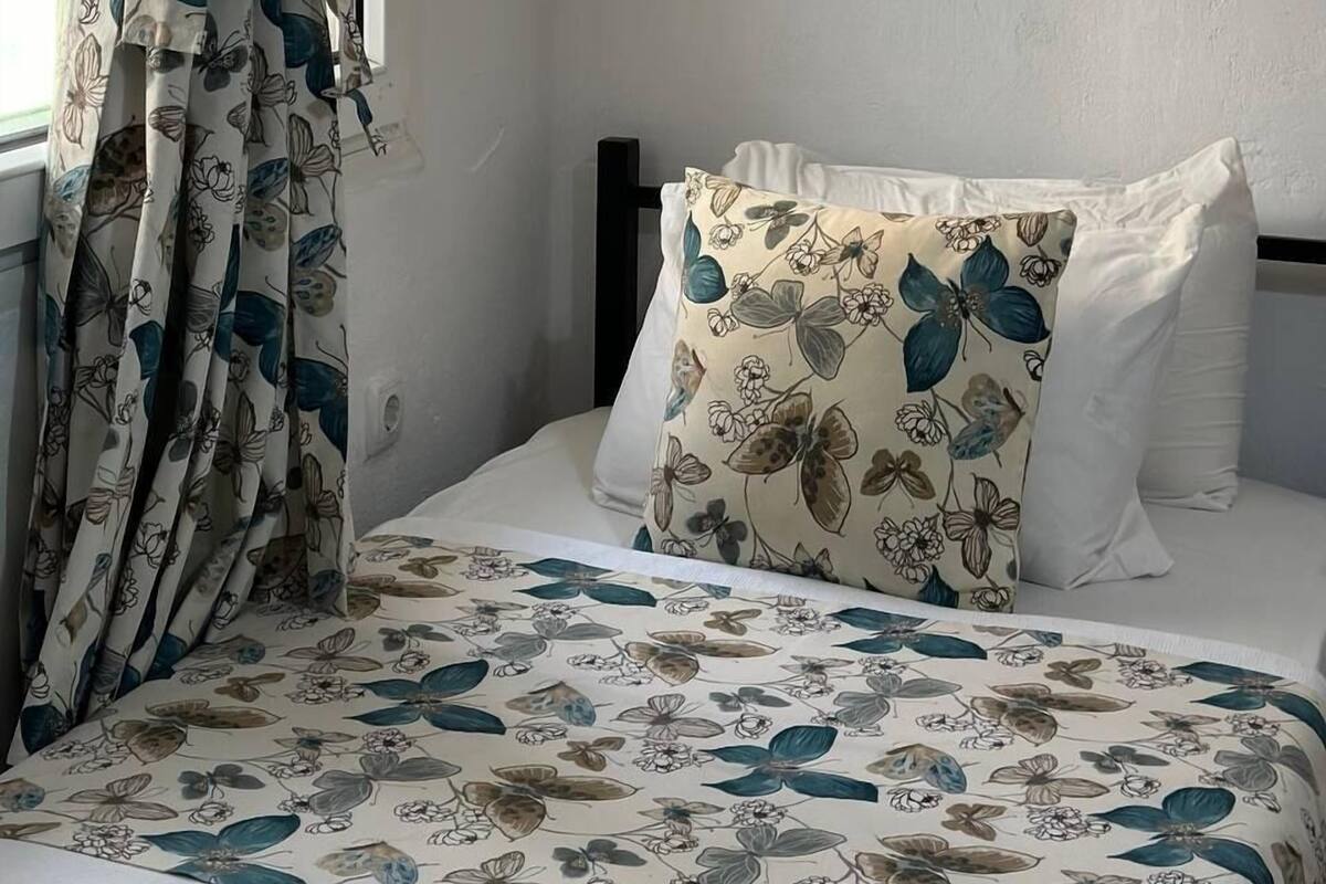 A bedroom with a bed, floral-patterned curtains, a pillow with a similar design, and a plain wall.