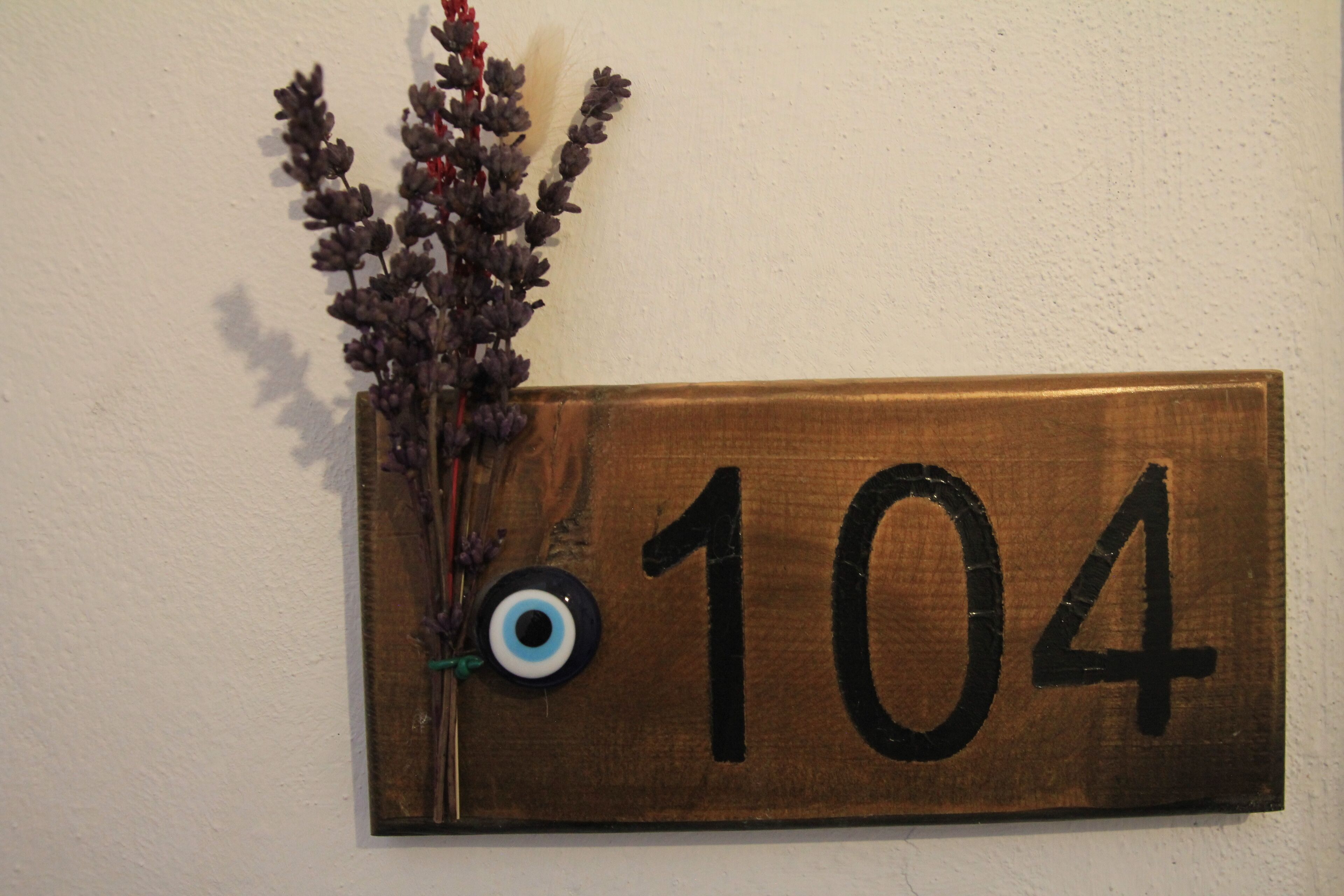 Una placa de madera con el número 104, un arreglo floral decorativo y un objeto pequeño azul y blanco.