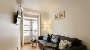 Una sala de estar con un sofá de cuero marrón, una mesita redonda y una lámpara. Se ve una puerta que da a otra habitación.