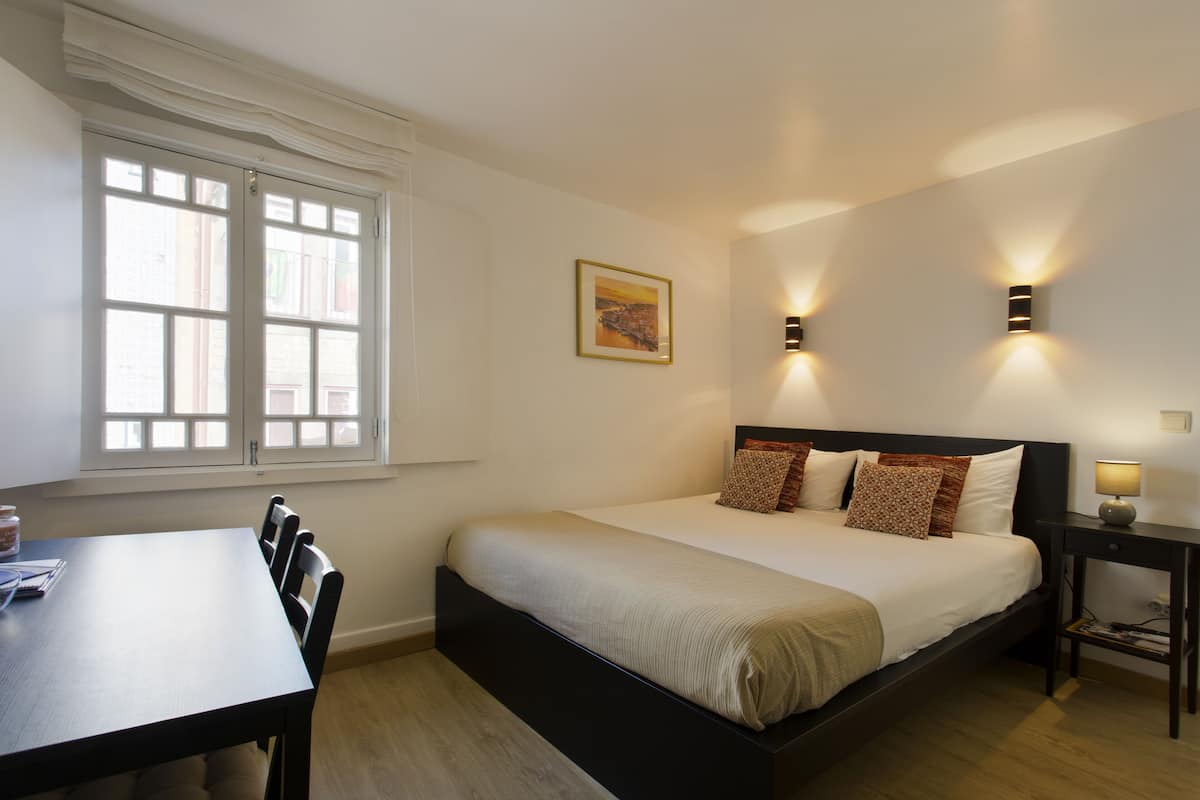 Een slaapkamer met een bed, nachtkastje, lamp en een raam met gordijnen.