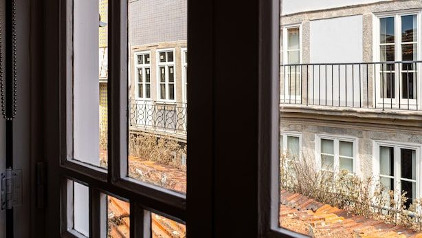 Vista a través de una ventana que muestra un edificio con una torre de reloj, varias ventanas y un balcón.