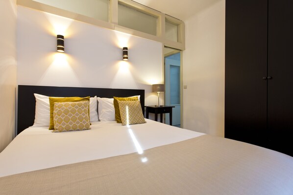 A modern bedroom with a large bed, two wall-mounted lights, a nightstand, and a wardrobe.