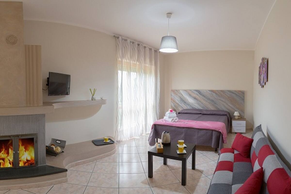 Una habitación de hotel moderna con chimenea, una cama, un sofá y un televisor.