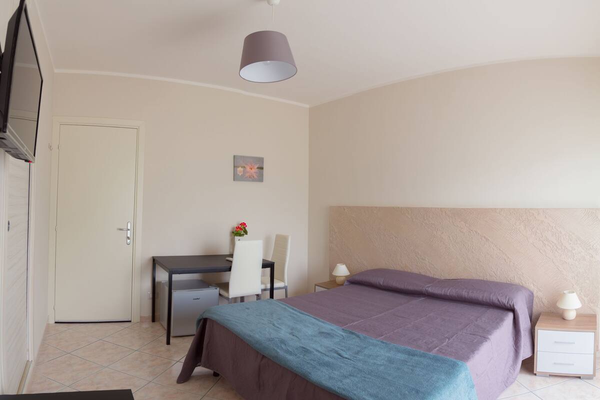 Habitación de hotel con dos camas, un escritorio, una silla, una mesita, una lámpara y un televisor.
