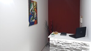 A room with a white desk, a laptop, a framed painting, and a red accent wall. - B&B La Perla dei Casali (Giffoni sei Casali)