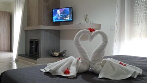 A hotel room with a bed, a TV on the wall, a fireplace, and a heart-shaped towel decoration. - B&B La Perla dei Casali (Giffoni sei Casali)