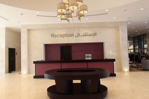 A reception area with a marble wall, a reception desk, and a modern chandelier. - Normas Hotel (Al Khobar)
