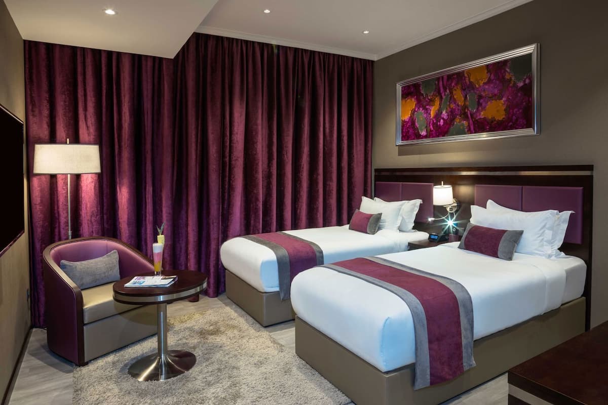 A hotel room with two beds, a desk, a chair, a TV, and a painting on the wall.