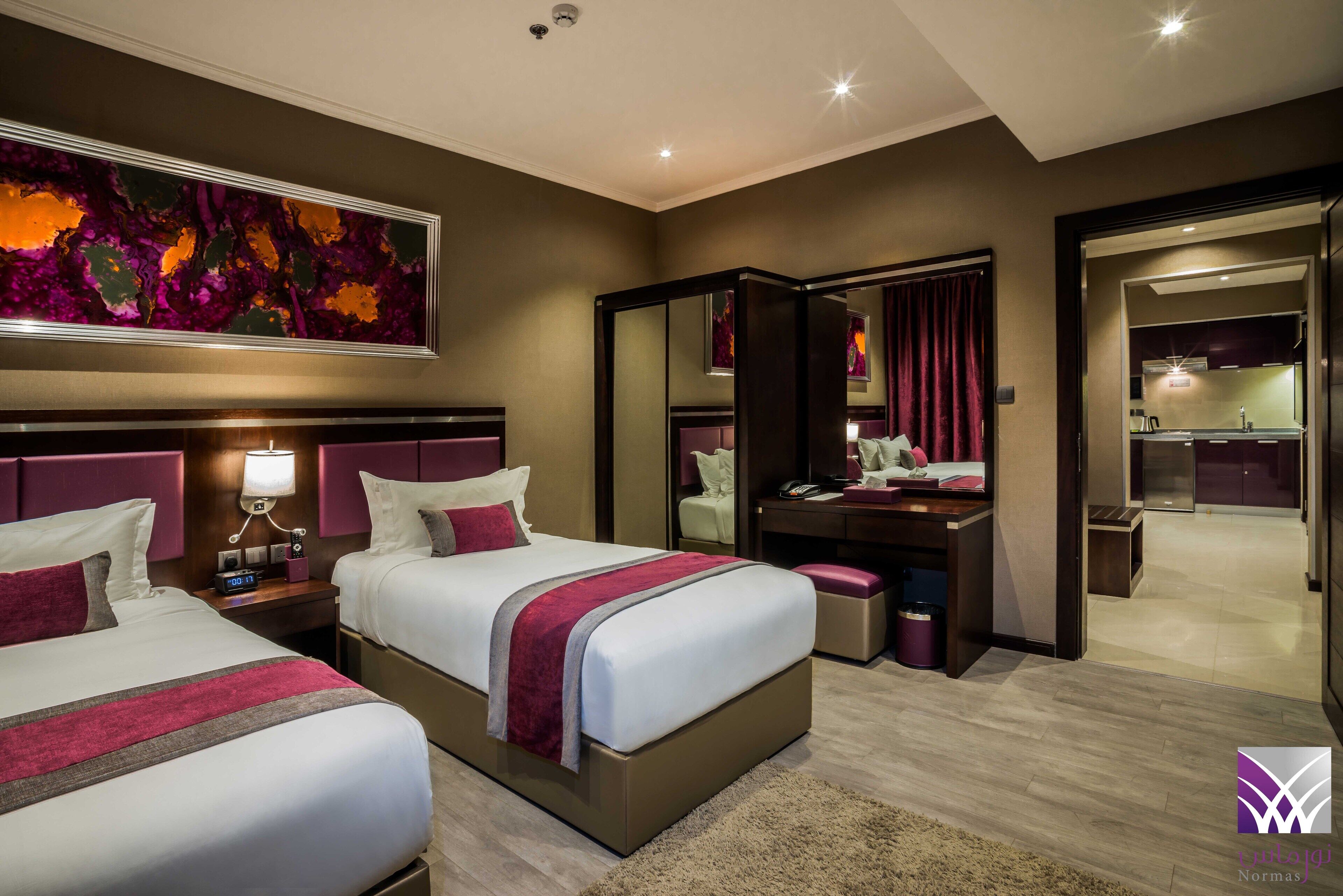 Ein Hotelzimmer mit zwei Betten, einem Schreibtisch, einem Spiegel und einem großen abstrakten Gemälde an der Wand.