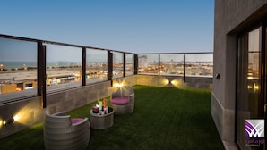 A rooftop terrace with a view of the cityscape, featuring wicker chairs and a small table with drinks. - Normas Hotel (Al Khobar)
