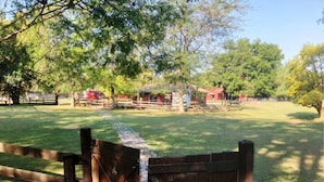 Een omheind terrein met een houten poort, gazons en bomen.