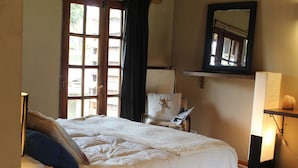 Een slaapkamer met een bed, een stoel, een bureau, een lamp en een raam met gordijnen.