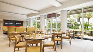 A hotel lobby with round tables and chairs, a sofa, and a large window offering a view of the outdoors. - Hotel Continental Miami Beach, Tapestry Collection by Hilton (Miami Beach)