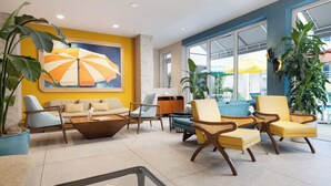 A modern lobby with a yellow accent wall, a large abstract painting, and a seating area with yellow and blue chairs. - Hotel Continental Miami Beach, Tapestry Collection by Hilton (Miami Beach)