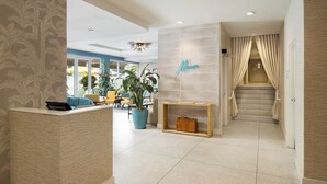 A hotel lobby with a reception desk, seating area, staircase, and a wall with a name sign. - Hotel Continental Miami Beach, Tapestry Collection by Hilton (Miami Beach)