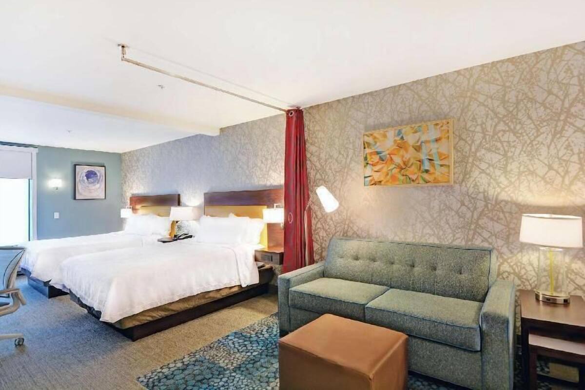 A hotel room with a bed, a sofa, a desk, and a lamp.