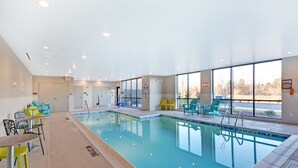 Una piscina interna con acqua cristallina, circondata da sedie e tavoli.