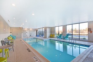 Una piscina interior con agua cristalina, rodeada de sillas y mesas.
