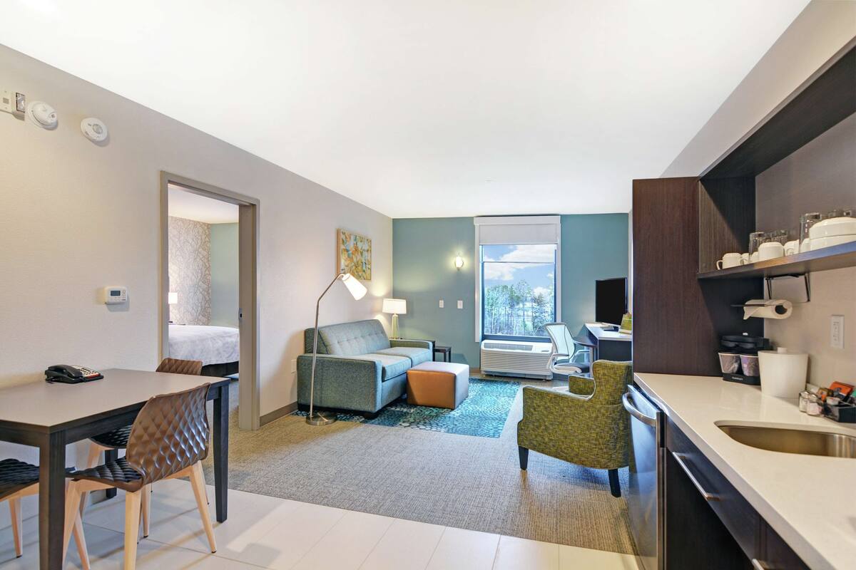 A compact hotel room with a dining area, a sofa, a small table, and a kitchenette.