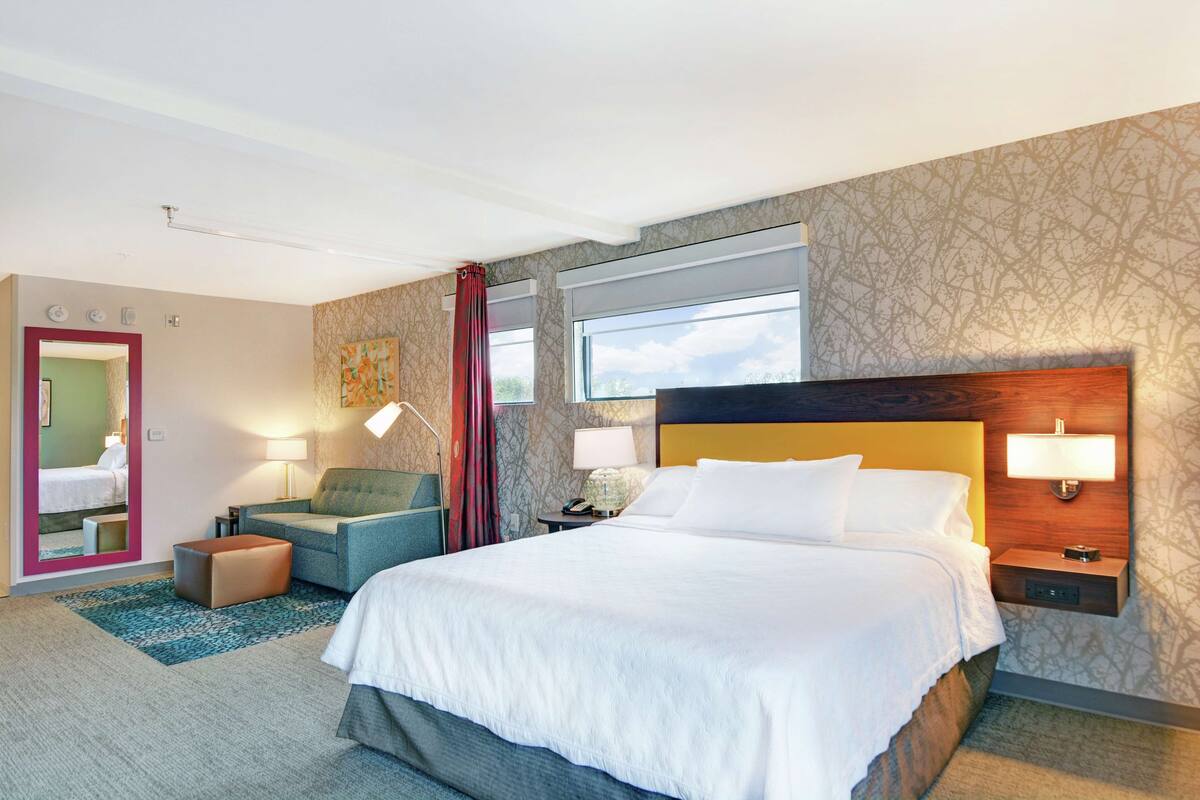 A hotel room with a large bed, a sofa, a desk, and a window with a view.