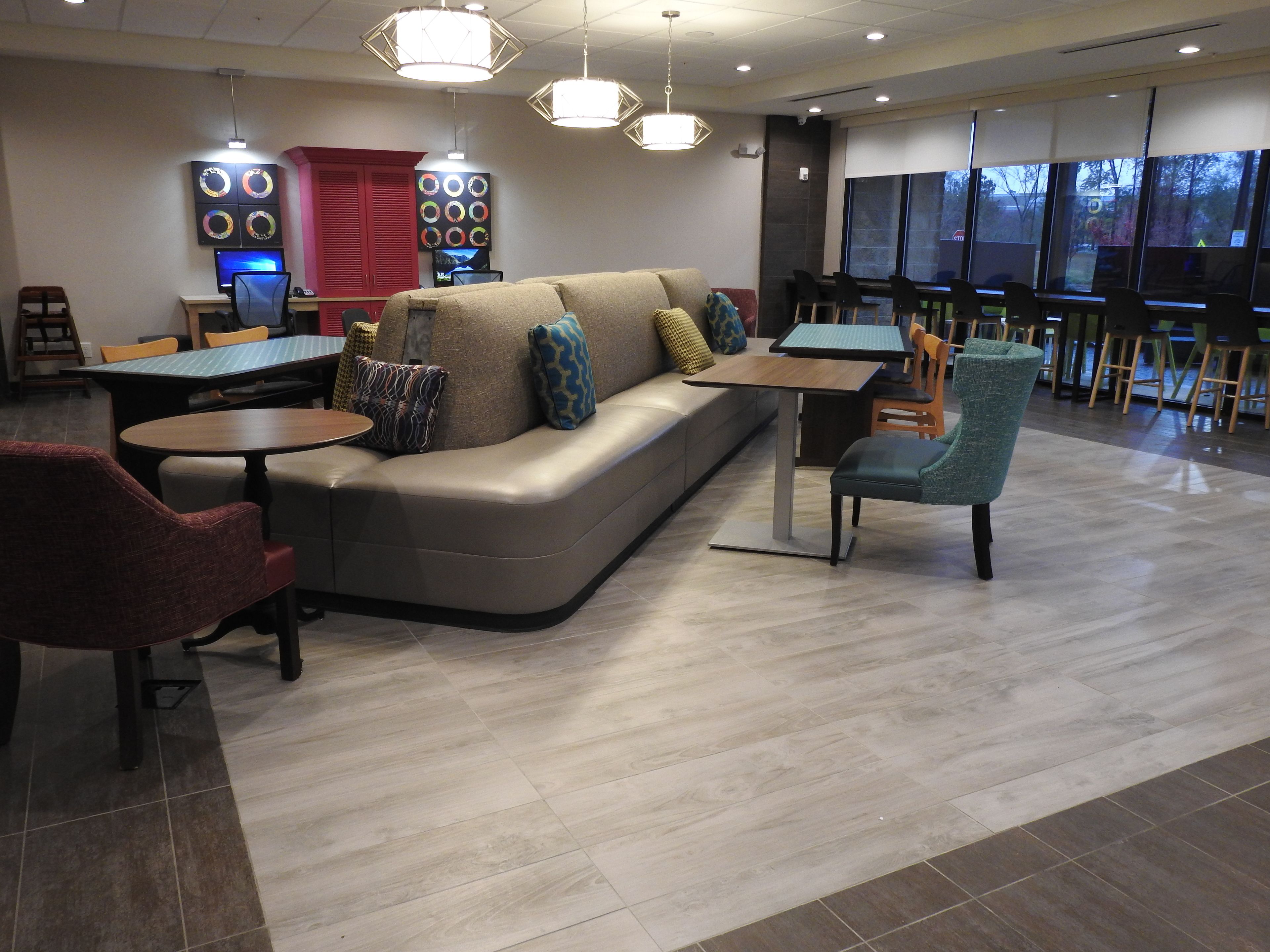 A modern lounge area with a sofa, tables, chairs, and a TV screen.