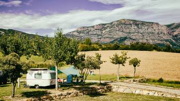 Un terrain de camping avec une caravane, un camion et un champ en arrière-plan.