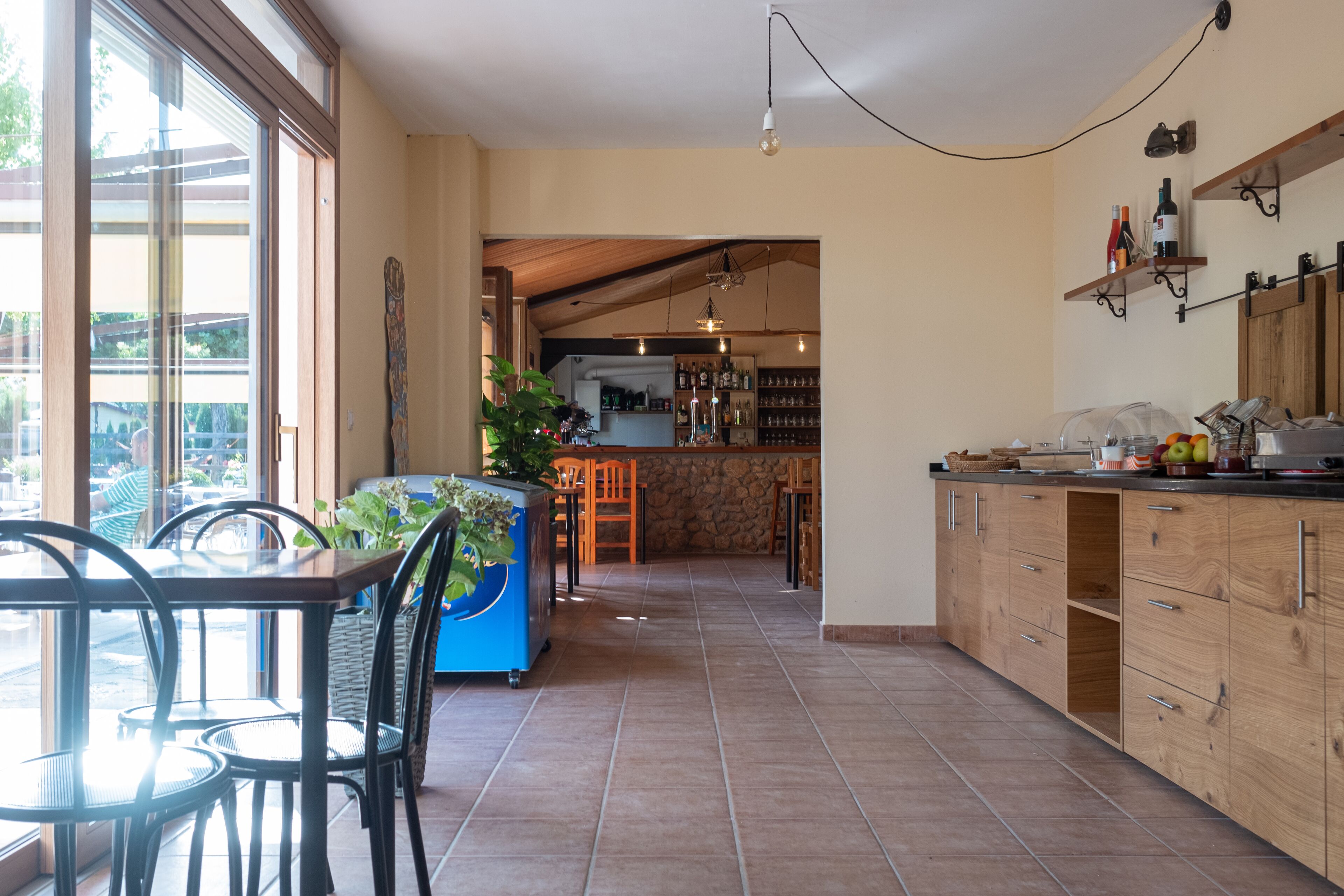 A spacious kitchen with wooden cabinets, a dining area with chairs, and a view through large windows.