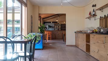 A spacious kitchen with wooden cabinets, a dining area with chairs, and a view through large windows.
