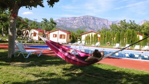 A hammock by a pool with lounge chairs, a lifebuoy, and houses in the background. - Camping Bungalow Parque Isábena (Isabena)