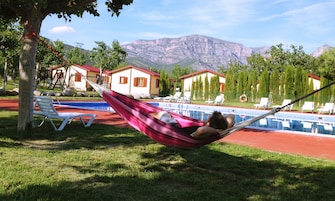 Una hamaca junto a una piscina con sillas de descanso, un flotador y casas al fondo.