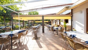 An outdoor patio with multiple tables and chairs, covered by a yellow canopy, and surrounded by greenery. - Camping Bungalow Parque Isábena (Isabena)