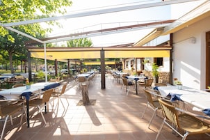 Un patio al aire libre con varias mesas y sillas, cubierto por un toldo amarillo y rodeado de vegetación.
