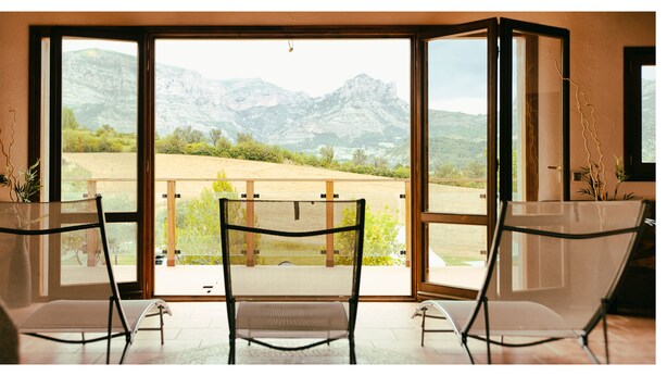 A room with a large sliding glass door leading to a balcony with a mountain view. There are two chairs and a small table on the balcony. - Camping Bungalow Parque Isábena (Isabena)