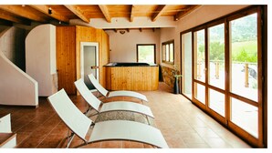 A modern interior with a wooden bar, white chairs, and large windows offering a view of the outdoors. - Camping Bungalow Parque Isábena (Isabena)