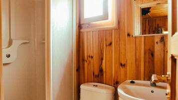 A compact bathroom with wooden walls, a white toilet, a sink, and a shower enclosure.