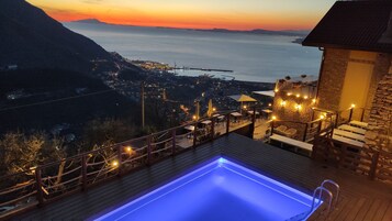 Zona de piscina con vista al mar y un paisaje urbano lejano al atardecer.