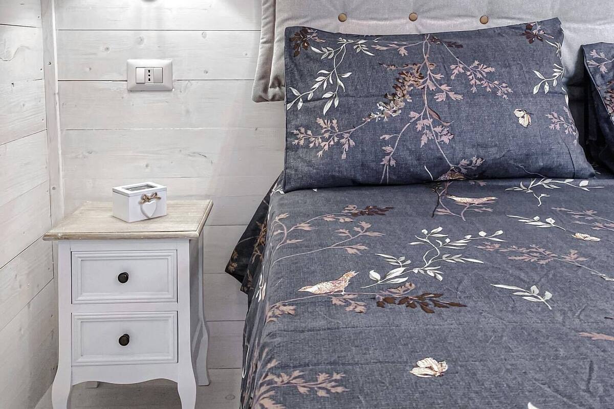 A bedroom with a bed, a nightstand, a lamp, and a wall socket.