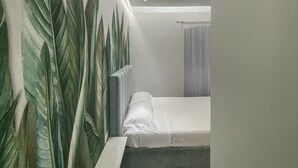Un dormitorio con cama, mesita de noche y pared con un estampado de hojas grandes.