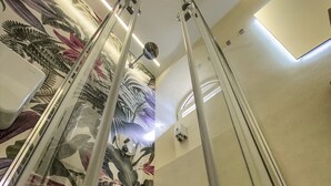 Un baño moderno con cabina de ducha de vidrio, un mural floral en la pared y una lámpara en el techo.