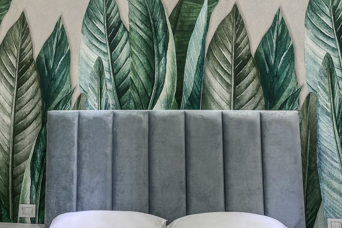 A bedroom with a headboard featuring a large, leafy pattern and a neutral-toned bed.
