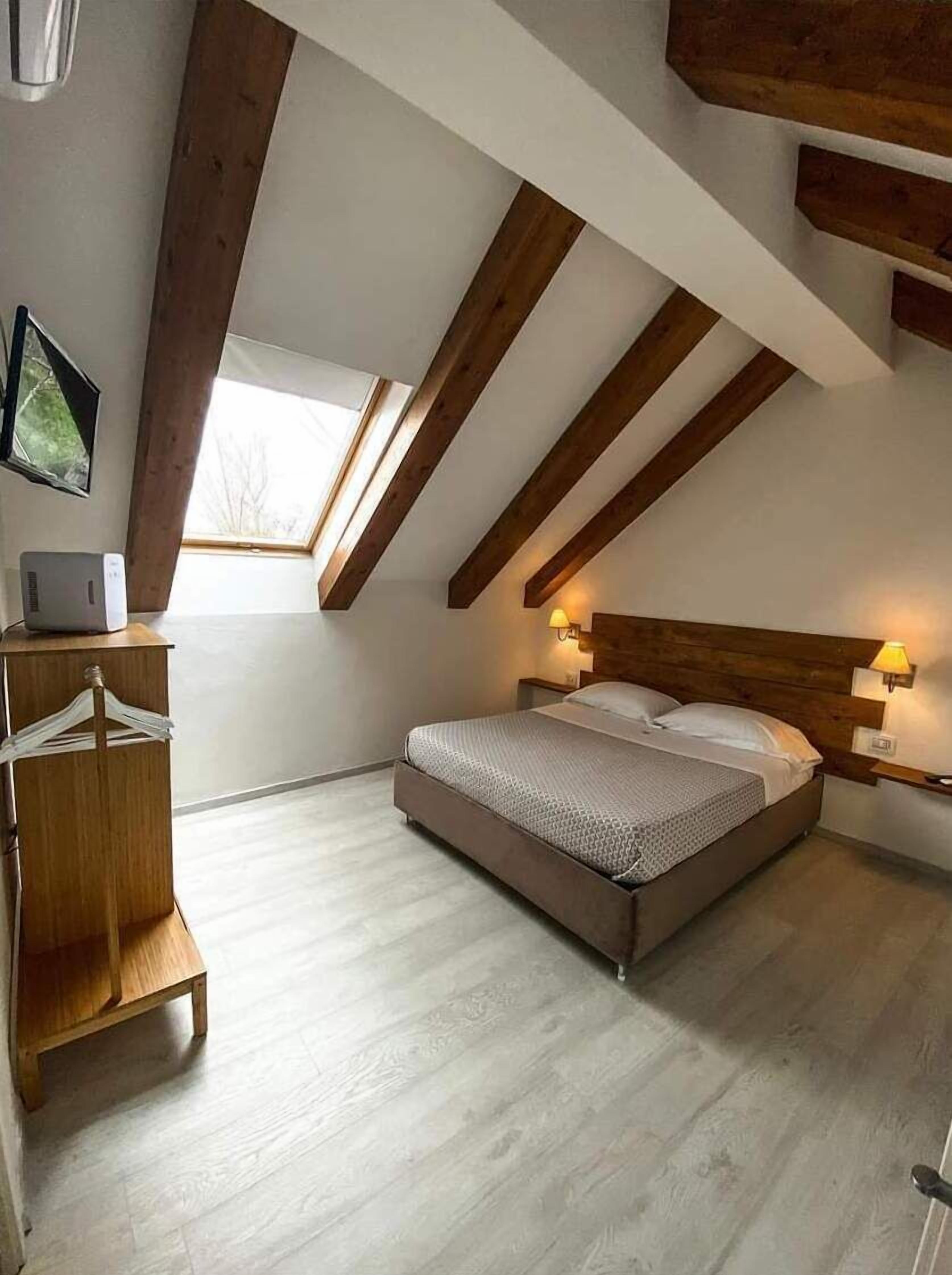 A bedroom with a sloped ceiling, a bed, bedside lamps, a wooden dresser, and a window.
