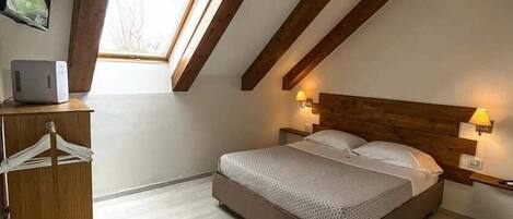 A bedroom with a sloped ceiling, a bed, bedside lamps, a wooden dresser, and a window.