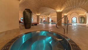 Amplia zona de piscina interior con vista despejada, columnas de piedra y techos abovedados.