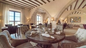Un área de comedor con una mesa redonda dispuesta para cuatro personas, rodeada de sillas tapizadas. La habitación cuenta con techos abovedados con vigas de madera a la vista y amplios ventanales que dejan entrar la luz natural.