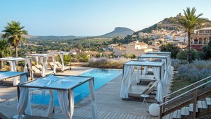 Una terraza de madera con tumbonas y piscina, con vistas a un pueblo en la ladera.