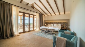 Un dormitorio amplio con una cama grande, dos mesitas de noche y una mesita auxiliar, con vistas a un espacio exterior a través de una puerta corrediza de vidrio.