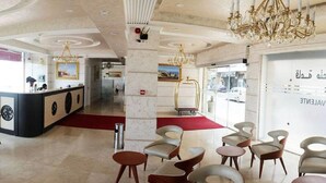 Un vestíbulo de hotel con mostrador de recepción, zona de estar, candelabros y un amplio ventanal con texto.