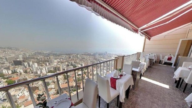 A balcony with tables and chairs, overlooking a cityscape. - Ikram el Dhayf (Algiers)