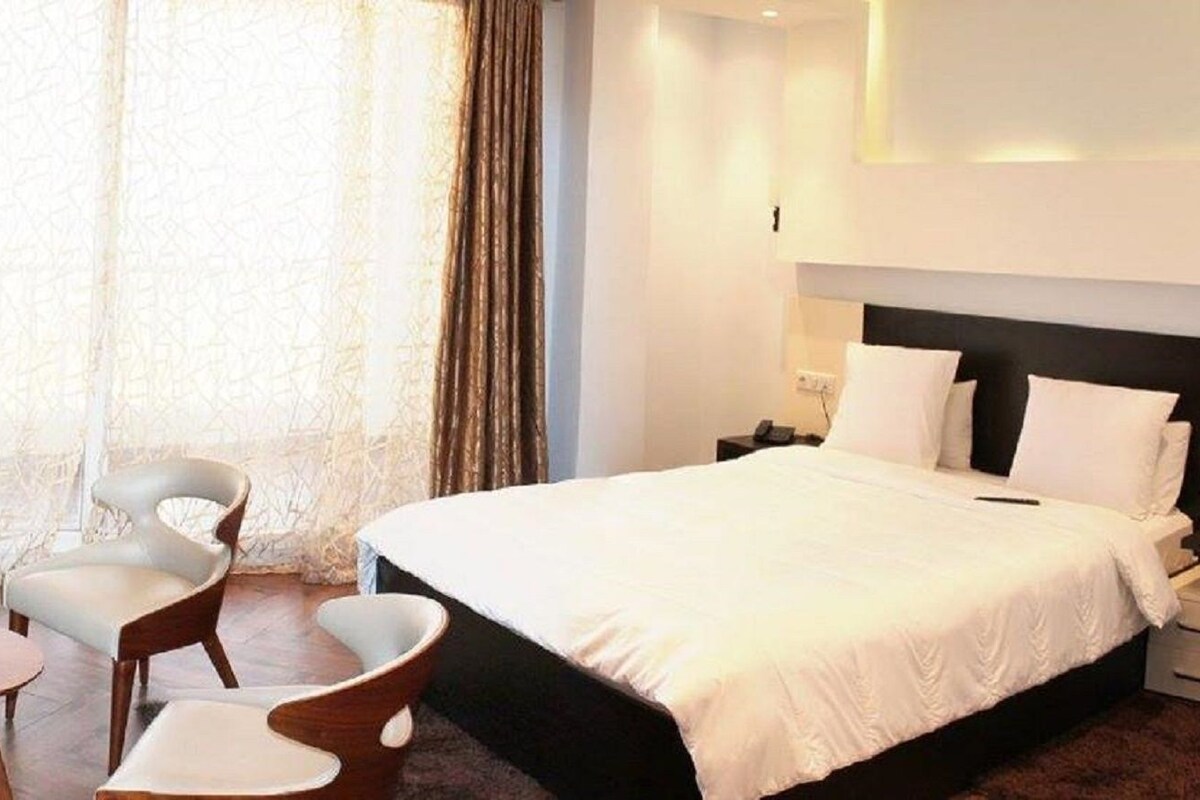 A hotel room with a large bed, two chairs, a small table, and a nightstand with a lamp.